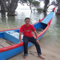 Nabil Berri, Acehnese language activist, photographed while leaning on a wooden boat by a river.